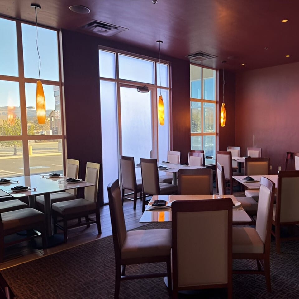 Jazmine restaurant interior with modern tables, chairs, and large windows with hanging orange lights.