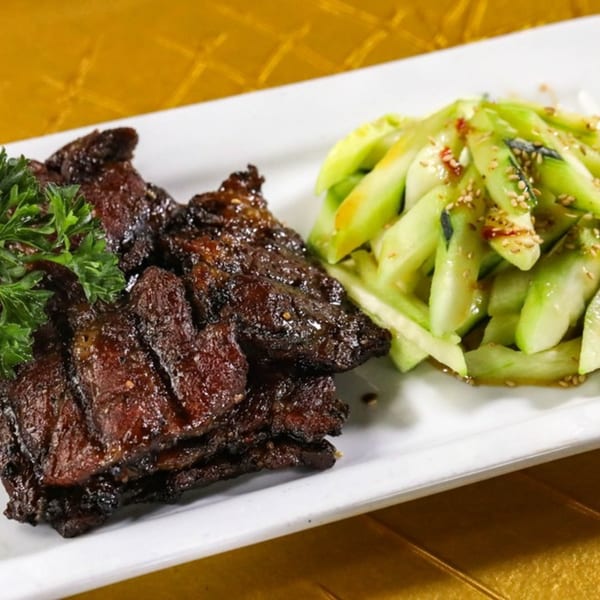 Jazmine's Asian cuisine features dark, glazed meat slices with fresh green cucumber salad and sesame seeds.
