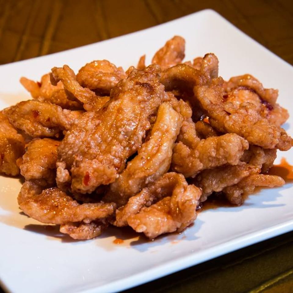 A white rectangular plate filled with crispy, golden-brown Jazmine Asian chicken strips coated in a sweet sauce.