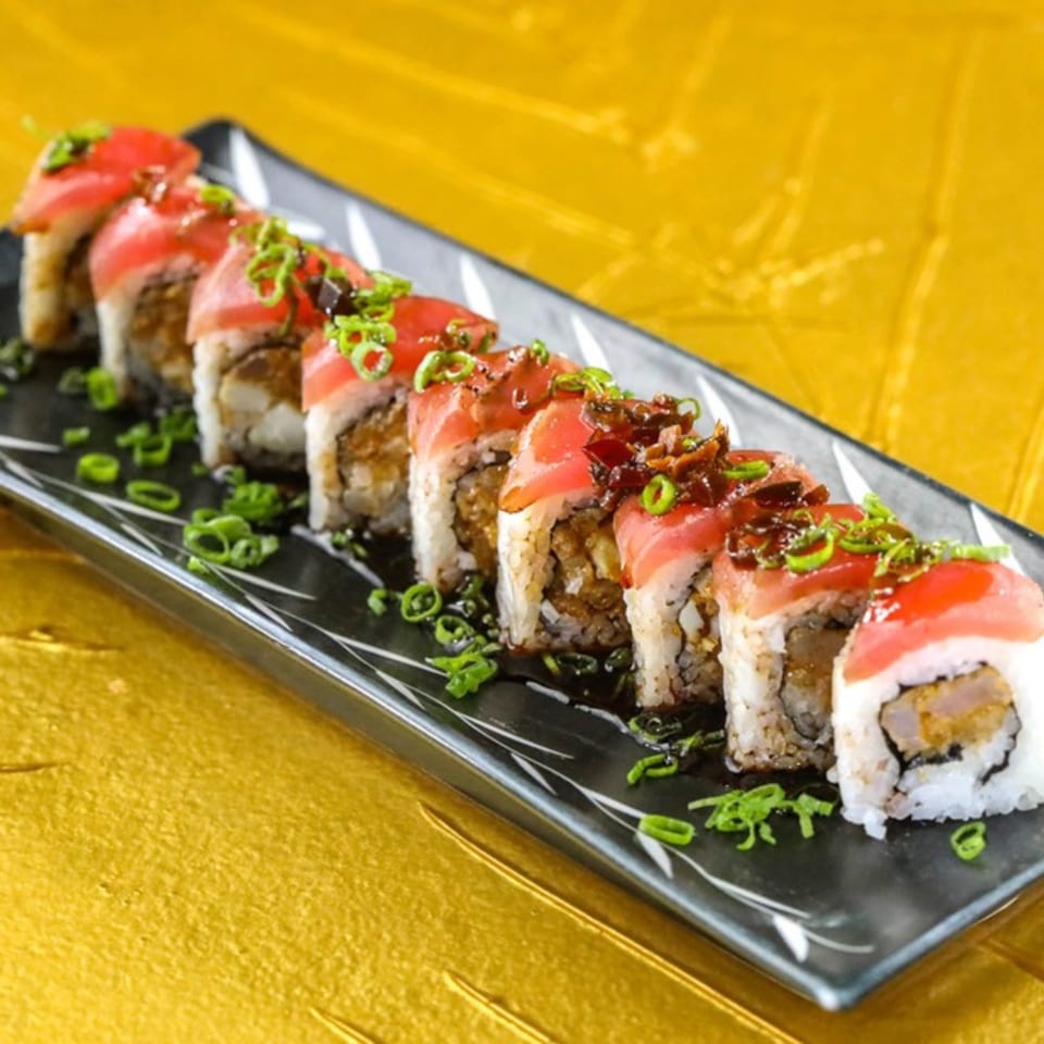A black rectangular plate holds eight pieces of Jazmine's tuna sushi rolls, garnished with green onions.