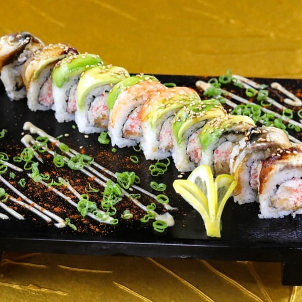 A row of Jazmine sushi rolls with avocado, shrimp, and eel, garnished with scallions and lemon.