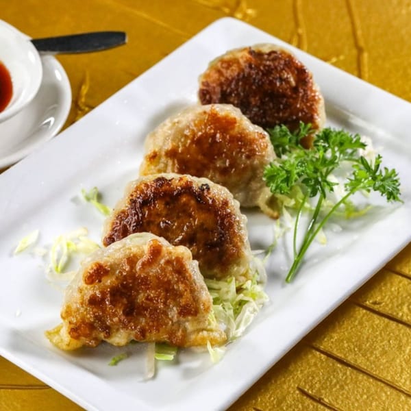Four pan-fried Jazmine dumplings with crispy bottoms, garnished with parsley and shredded cabbage.
