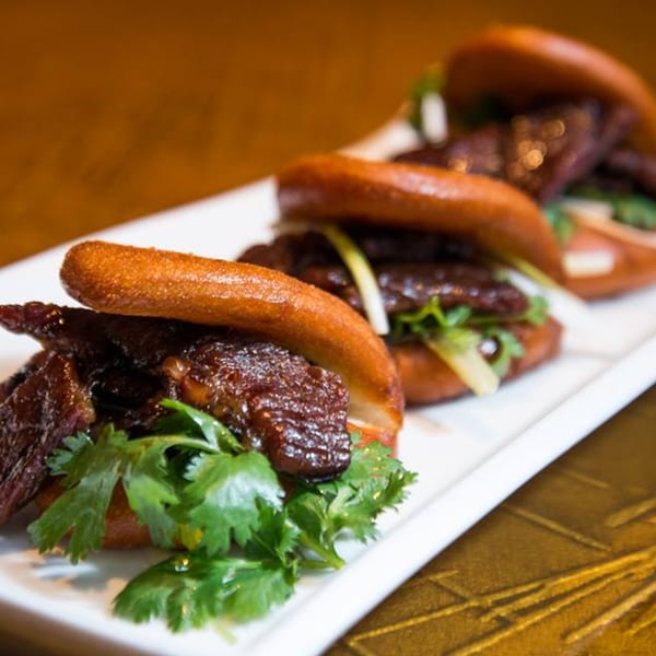 Three Jazmine Asian restaurant bao buns with glazed meat and fresh cilantro on a white plate.