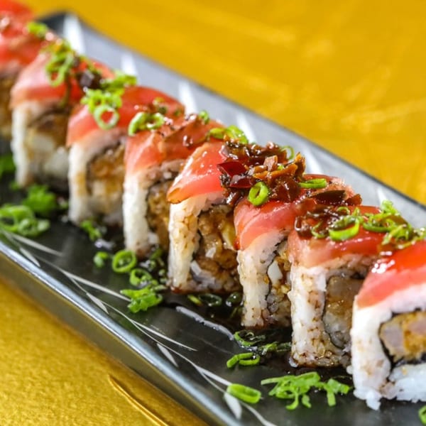 Jazmine's sushi rolls with tuna, green onions, and a dark sauce on a black plate.