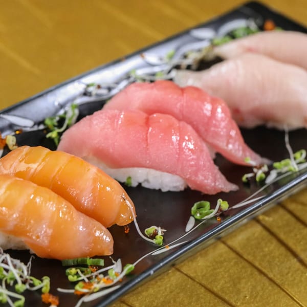 A black rectangular plate holds various nigiri sushi, including salmon, tuna, and white fish.