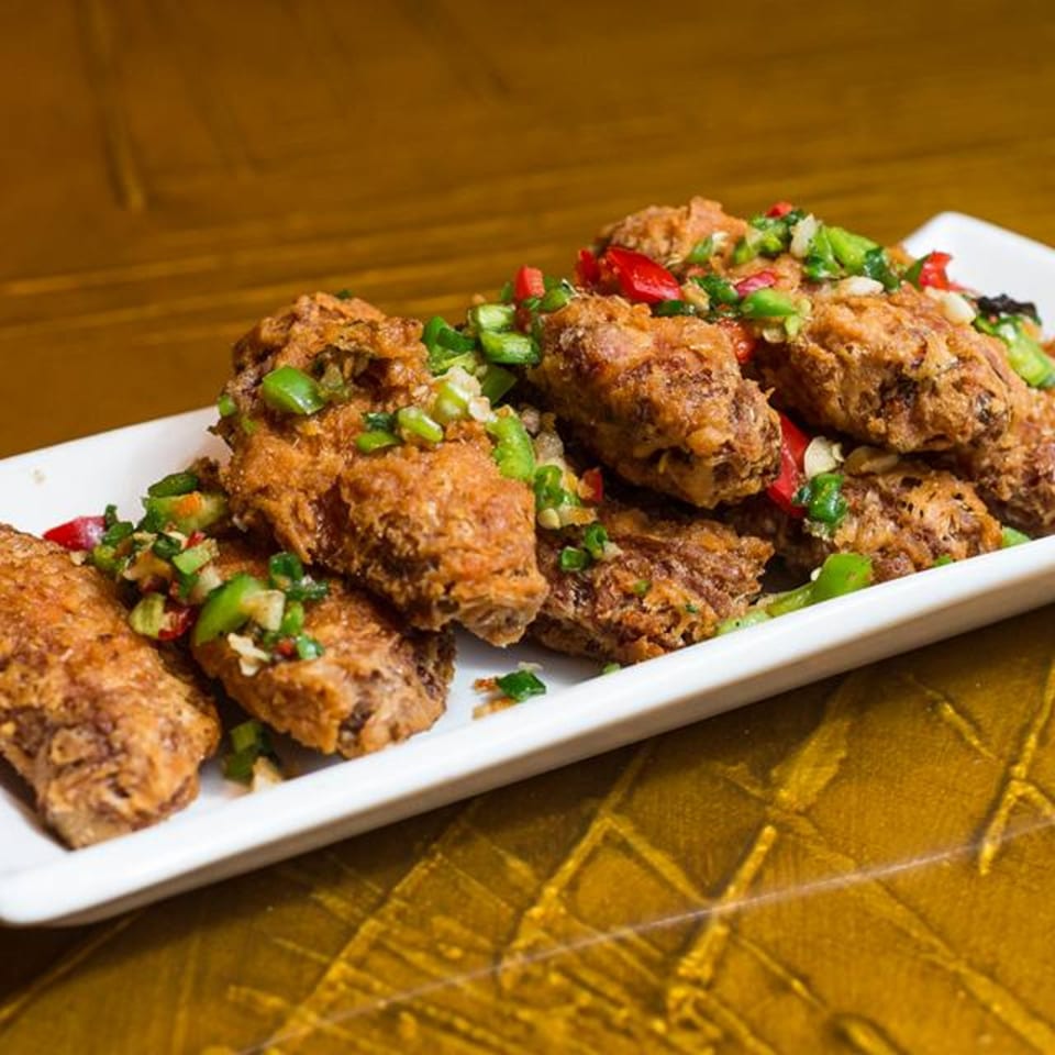 Crispy fried chicken wings topped with diced green and red peppers on a white rectangular plate.