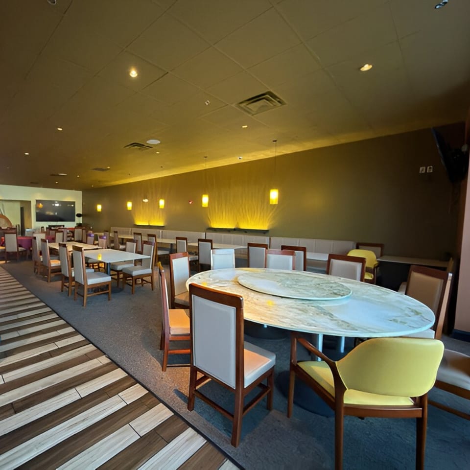 Spacious Jazmine dining room with round and rectangular tables, wooden chairs, and warm wall lighting.